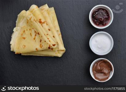 pile of french pancakes on dark background with sugar, chocolat and jam on little jar
