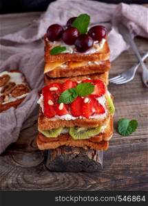 pile of French toast from white bread with cottage cheese, strawberries, kiwi, cherries on a gray wooden board