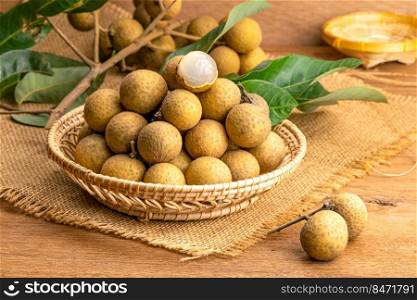 Pile of fresh langan in bamboo basket with bunch of longan and green leaves place on sack cloth on wooden table.