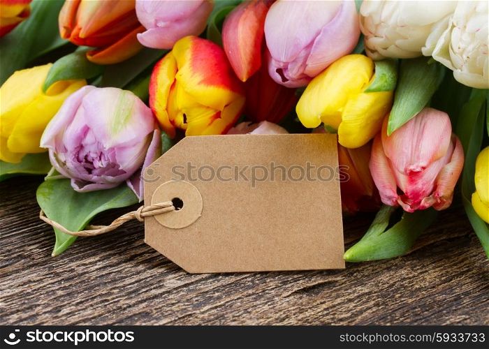 pile of fresh muticolored tulips with empty tag on aged wooden table with copy space. pile of multicolored tulips