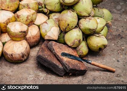 Pile of fresh sweet coconuts and big cutting knife on stone with warm natural light