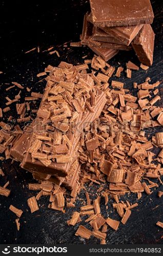 Pile of grated and pieces of milk chocolate. On rustic background. . Pile of grated and pieces of milk chocolate.