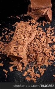Pile of grated and pieces of milk chocolate. On rustic background. . Pile of grated and pieces of milk chocolate.