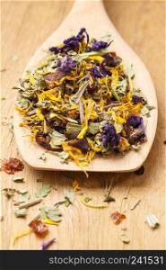 Pile of mixed natural medical dried herb leaves and flower petals on wooden spoon. . Pile of dry herb leaves and flower petals