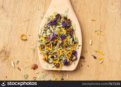 Pile of mixed natural medical dried herb leaves and flower petals on wooden spoon. . Pile of dry herb leaves and flower petals