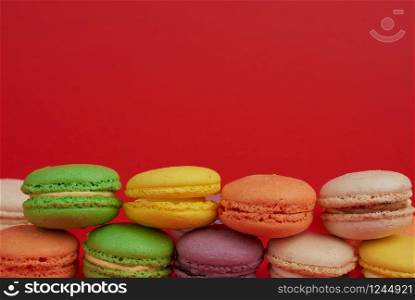 pile of multi-colored baked macarons almond flour cakes on a red background, copy space