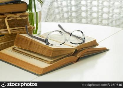Pile of old books with glasses on white table. Old books with rose flower