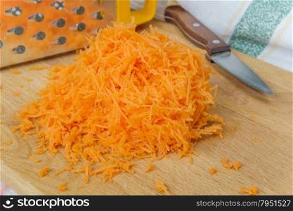 Pile of orange shredded carrots on a wooden cutting board