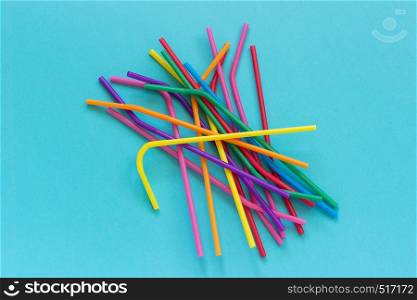 Pile of plastic disposable multi colored drinking straws for cocktails and drinks on blue background. Top view Copy space.. Pile of plastic disposable multi colored drinking straws for cocktails and drinks on blue background. Top view Copy space