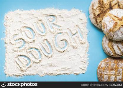 Pile of sourdough bread home baked and the word sourdough written in white flour. Above view with homemade bread on a blue background
