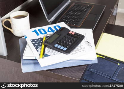 Pile of tax returns with computer, cup of coffee and calculator on desk
