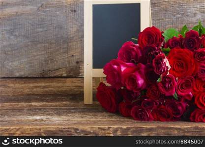 pile of vivd red and pink roses on wooden table with copy space on blackboard. pile of red roses