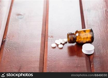Pile of white pills and glass bottle for medicines on a wooden background. Heap of white pills and glass bottle for medicines on a wooden background