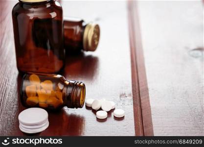 Pile of white pills and glass bottles for medicines on a wooden background. Heap of white pills and glass bottles for medicines on a wooden background