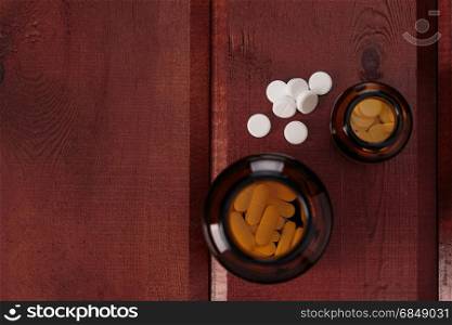 Pile of white pills and glass bottles for medicines.Top view. Heap of white pills and glass bottles for medicines on a wooden background