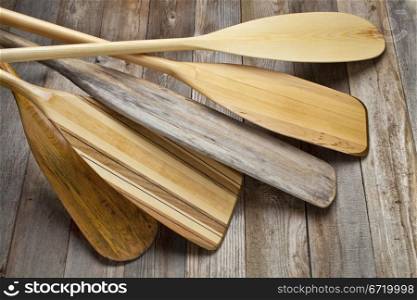 pile of wooden canoe paddles with different shapes and sizes of blades against grained wood deck
