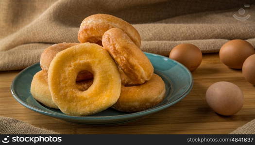 pile off fresh donuts in a plate with some eggs on background