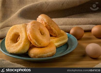pile off fresh donuts in a plate with some eggs on background