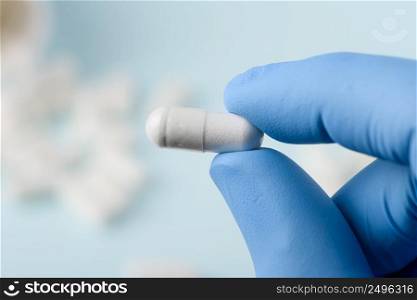Pill closeup in scientist hand with bottle on background