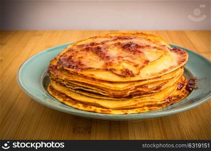 pille of fresh home made pancakes with strawberry jam in a blue plate over a wood table