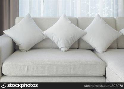 Pillows and sofa in beige color with sheer curtain in background