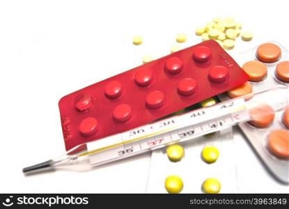 Pills, and thermometer close-up on white background