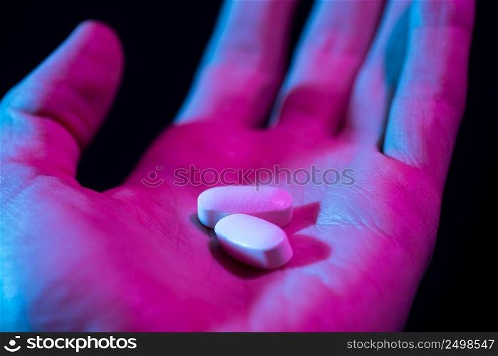 Pills in hand. Two drug tablets in palm close-up on dark background