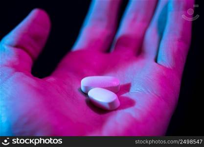 Pills in hand. Two drug tablets in palm close-up on dark background