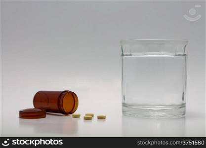 Pills spilling from bottle and a glass of water.