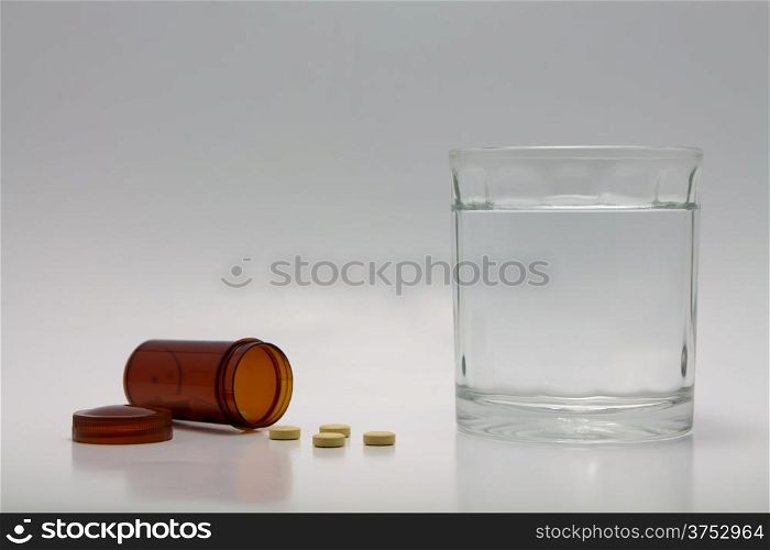 Pills spilling from bottle and a glass of water.
