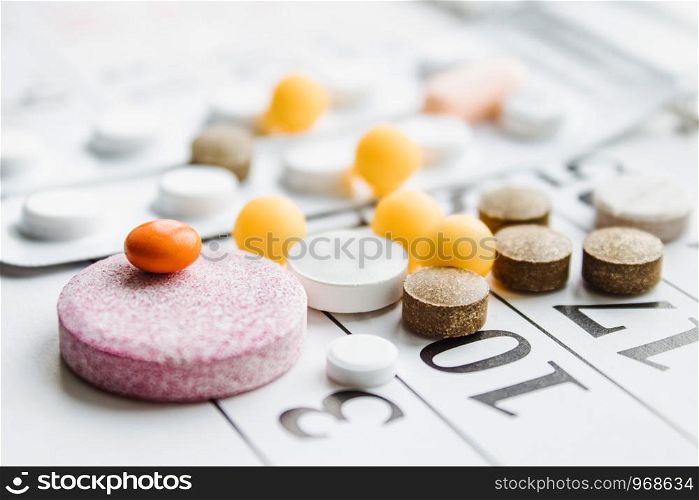 Pills, supplements and medicines for the disease. A pile of different pills on a calendar background. Healthcare. Pills, supplements and medicines for the disease. A pile of different pills on a calendar background.