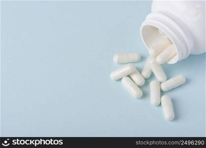 Pills with white powder in white plastic bottle on blue background with copy space