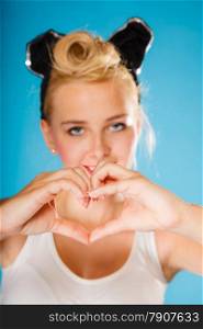 Pin up and retro style. Valentines day. Young smiling woman hairstyle making hands heart sign symbol on blue background.