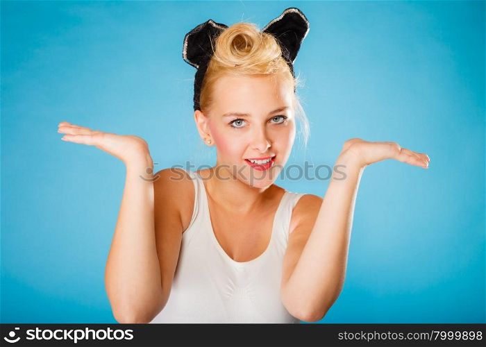 Pin up and retro style. Young smiling woman with black ears on head showing empty hands with copy space blue background.