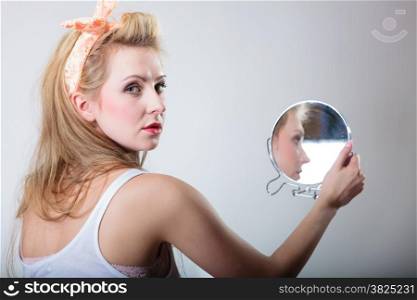 pin up beautiful blonde fashion girl in hairband looking at the mirror retro styling , studio shot gray background