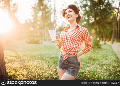 Pin up girl holds cardboard cup with a straw, city park on background. Vintage american fashion. Attractive woman in pinup style. Pin up girl holds cardboard cup with a straw
