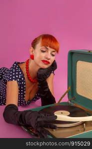 Pin-up model girl in retro polka-dot dress listens to an old gramophone on a pink background. girl listening to a gramophone