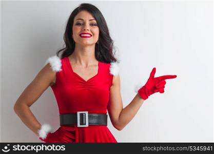 Pin-up Santa girl. Pretty Pin-up style Santa girl in red hat pointing to white background