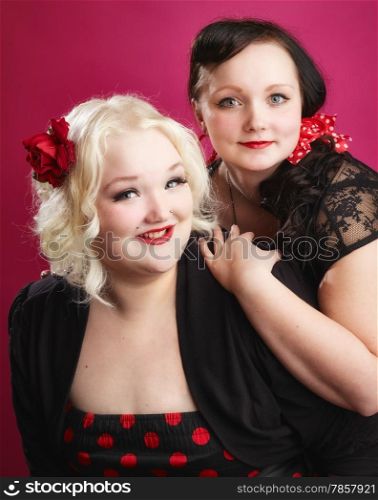 Pin-up sisters posing together and they looks toward the camera, pink background