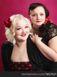 Pin-up sisters posing together and they looks toward the camera, pink background