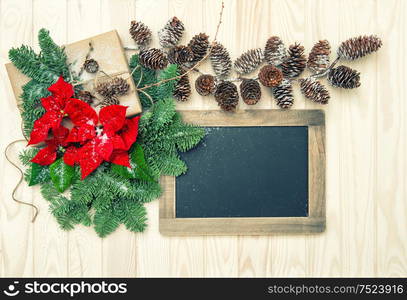 Pine branches with red flowers poinsettia and blackboard on wooden background. Christmas decoration. Vintage style toned picture