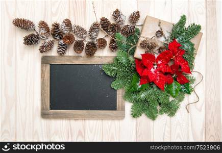 Pine branches with red flowers poinsettia and vintage chalkboard on wooden background. Christmas decoration