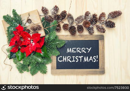 Pine branches with red flowers poinsettia decoration and blackboard on wooden background. Vintage style toned picture