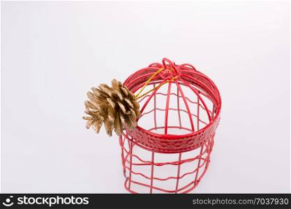 Pine cone in a red bird cage on a white background
