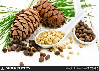 Pine nuts in two spoons, two cedar cones and green branches on a wooden board background