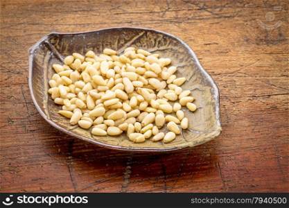 pine nuts on a ceramic, leaf shaped, bowl against rustic grunge wood surface