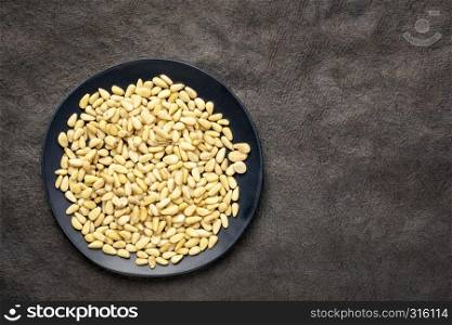 pine nuts with on a black plate, top view against black texture paper with a copy space
