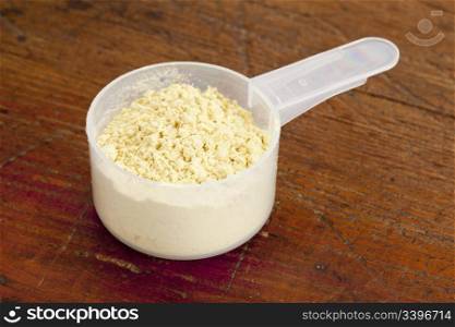 pine pollen powder (nutrition supplement) in a plastic measuring scoop against grunge wood surface