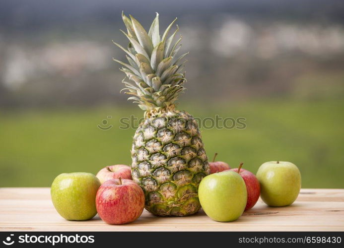 Pineapple and apple on wood table, outdoor