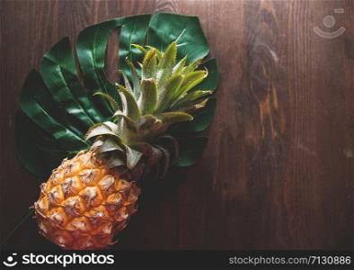 Pineapple and green leaf of monstera tree on wooden background top of view, selective focus